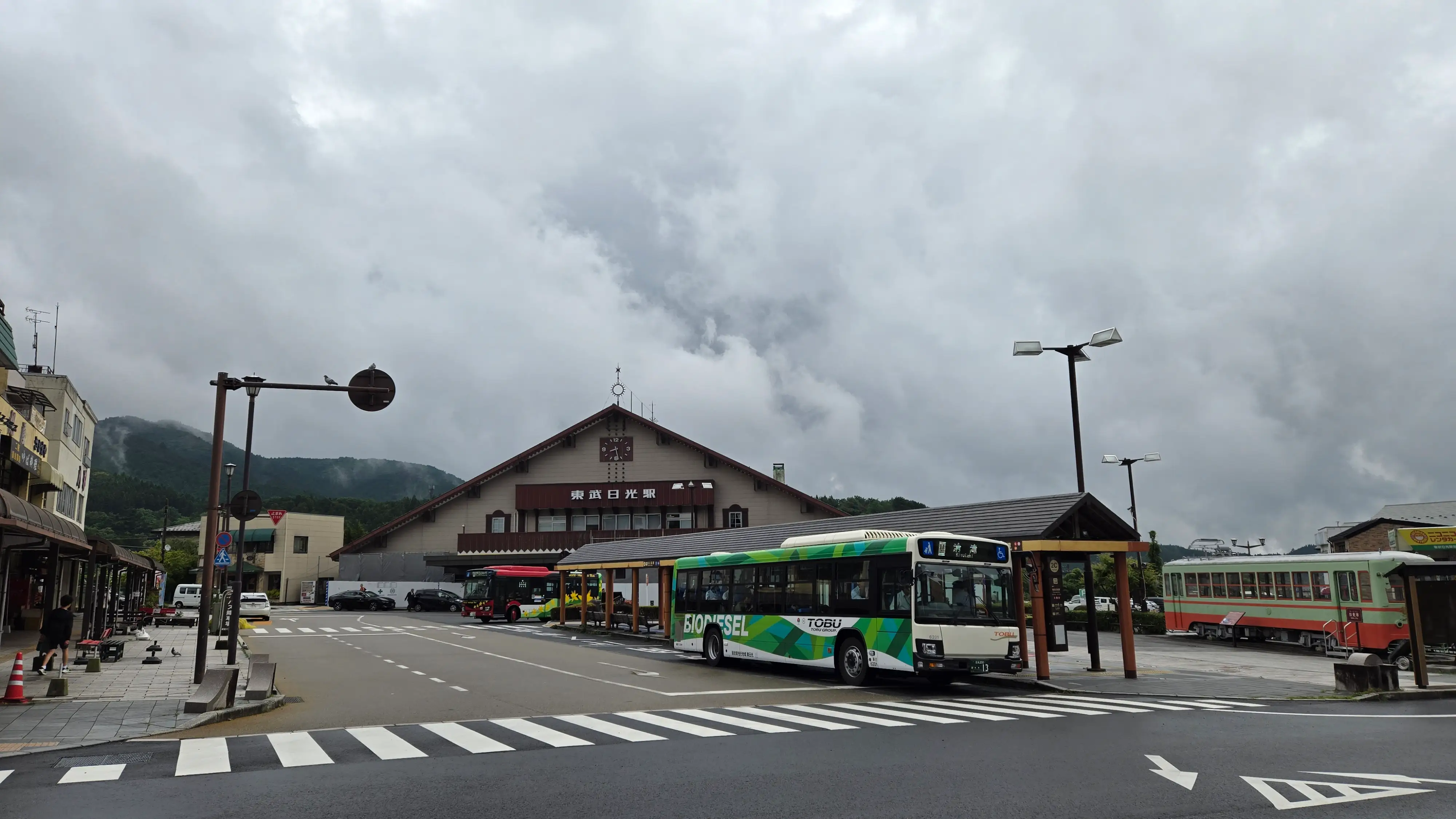 陰天的日光車站前廣場與巴士，以及通往山內的日光主街道，路邊是低矮的老店舖。