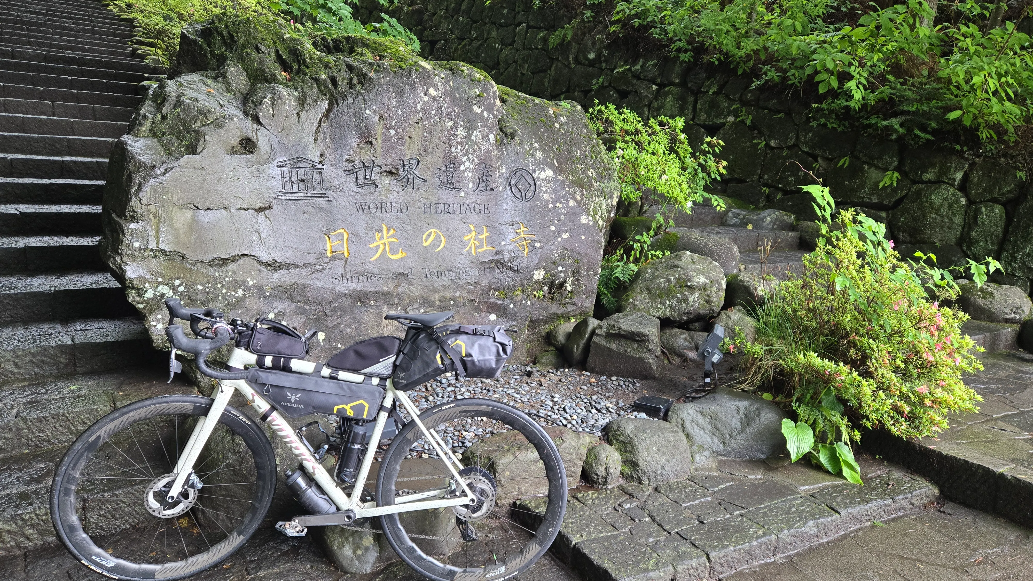 單車靠在刻著「世界遺產 日光的社寺」的石碑前，身後是石階與杉林。