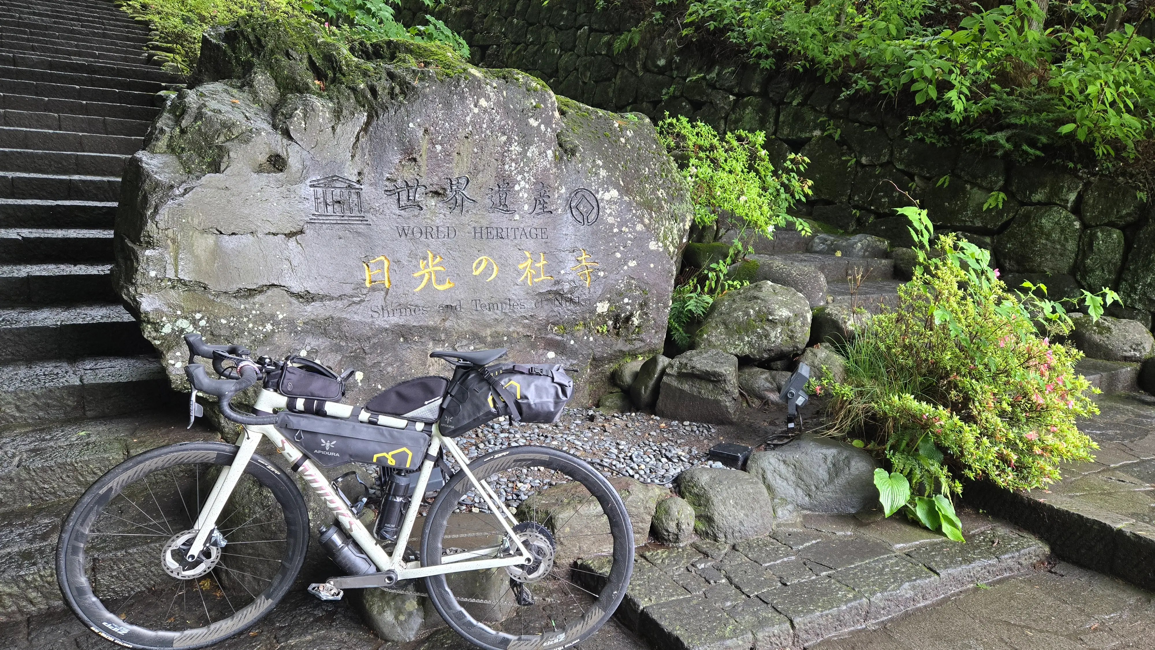 單車靠在刻著「世界遺產 日光的社寺」的石碑前，身後是石階與杉林。