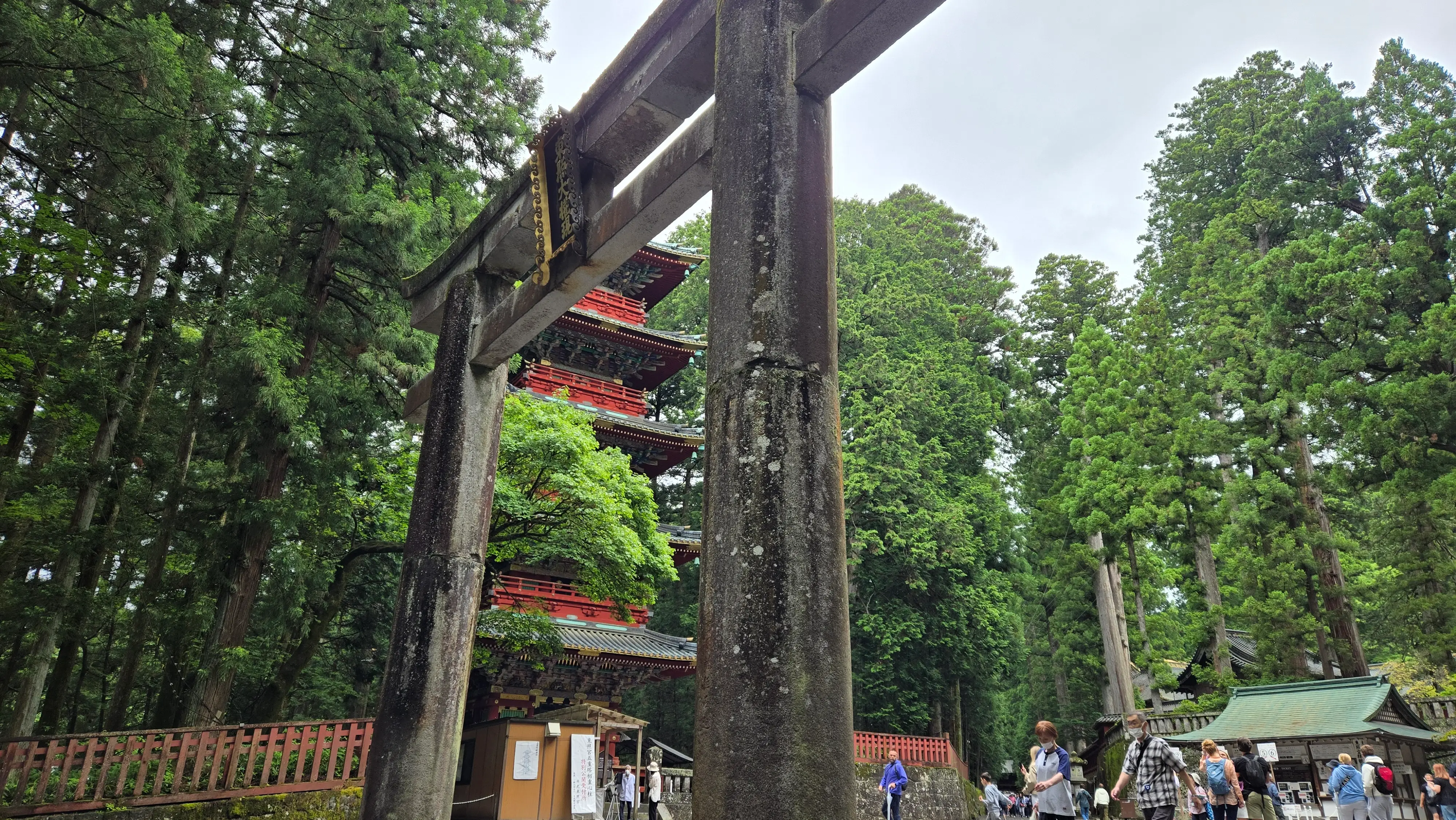 東照宮的石鳥居近拍，粗壯的石柱與橫梁，後方露出五重塔的一角。
