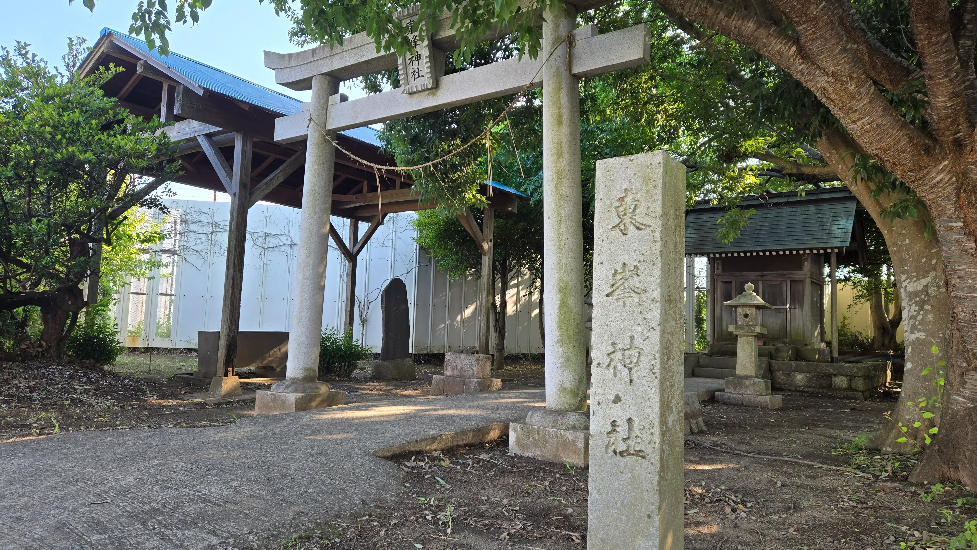 東峰神社的石造鳥居與刻著社名的石柱，後方是樹蔭下的神社。